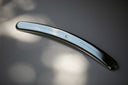 A silver-colored metal self-care tool with a curved and slightly concave shape, designed for use in self-treatment and scraping muscles.